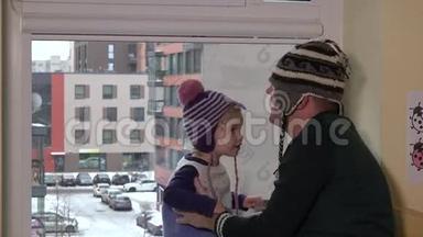 父亲和儿子戴着温暖的帽子，在窗户附近玩得很开心。 家人准备出门